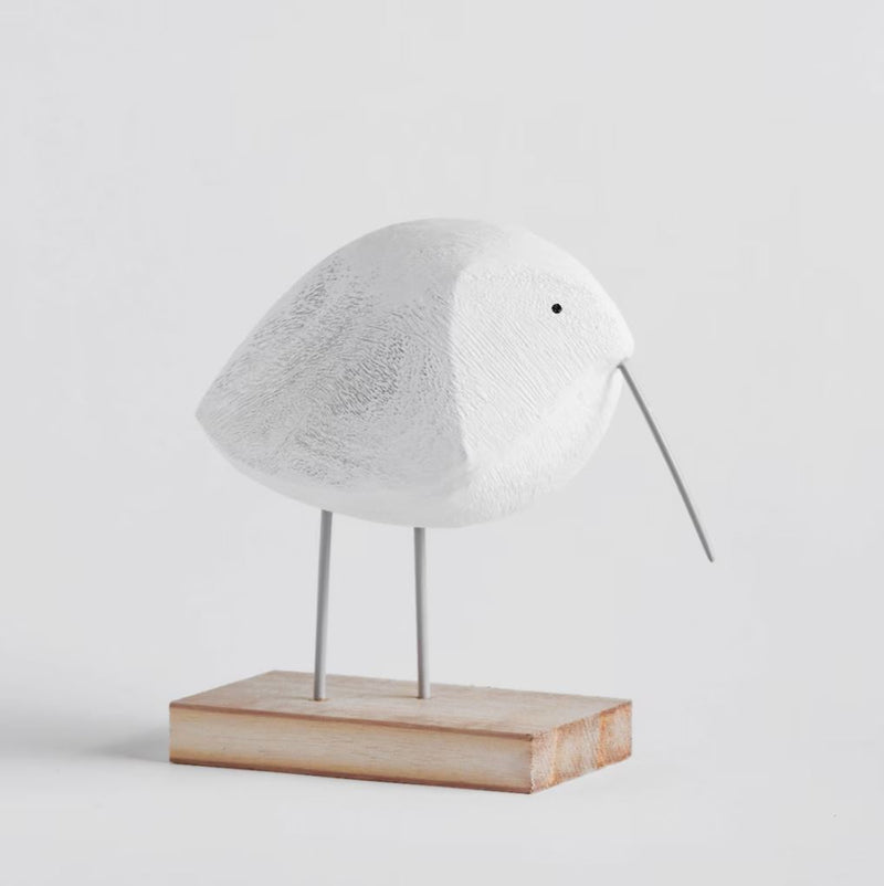 Biela figúrka v podobe vtáčika vyrobená z odolného polyresinu, ktorý hrdo stojí na drevenom podstavci. 